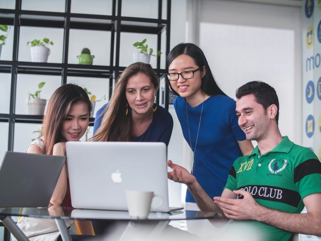 Four colleagues collaborating, smiling around a laptop